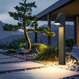 Strata Pro solar pathway light beside a stone path in a rock garden, washing warm light across the walkway at dusk
