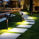 Strata Pro solar pathway lights lining a stepping stone walkway across a lawn at night, warm 3000K light pooling on each paver