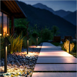 Strata Pro pathway lights along a paver walkway edged with river rock, lighting the path edge to edge at dusk